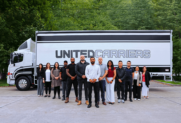 Group of twelve diverse people standing in front of a Brutelo Carriers truck outdoors.